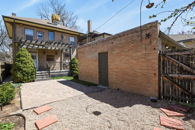 rear view of house featuring fence, a patio, a balcony, brick siding, and a gate