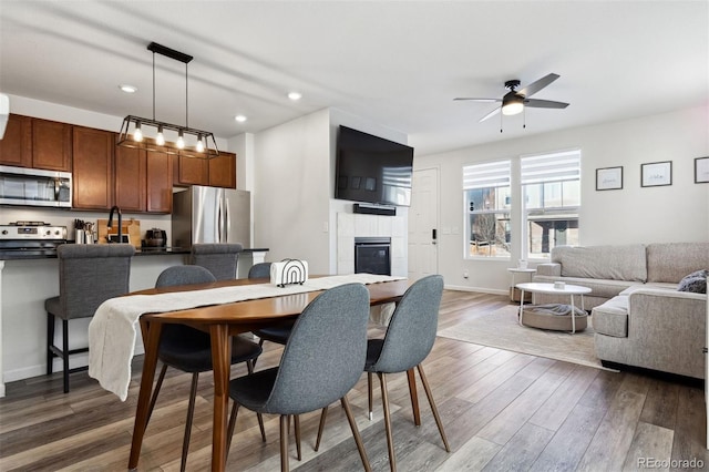 dining space with dark hardwood / wood-style flooring, ceiling fan, and a tiled fireplace