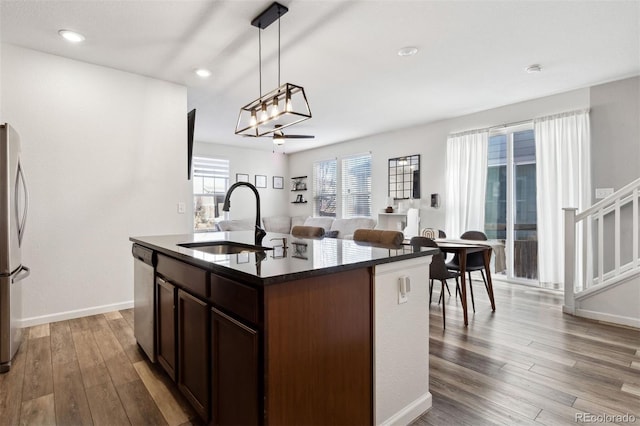 kitchen with dark brown cabinetry, sink, stainless steel appliances, pendant lighting, and a kitchen island with sink