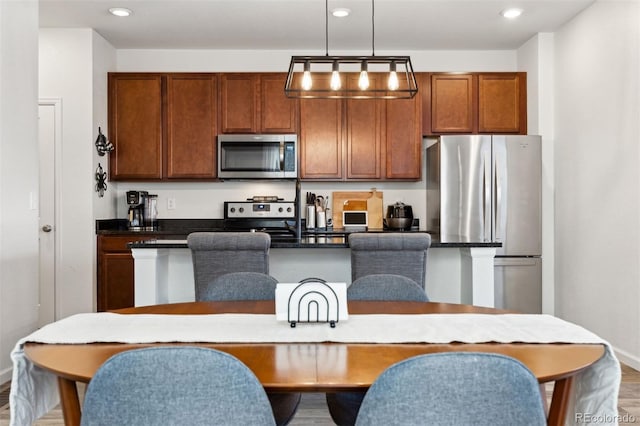 kitchen featuring hardwood / wood-style flooring, stainless steel appliances, hanging light fixtures, and an island with sink