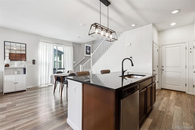 kitchen with stainless steel dishwasher, sink, a center island with sink, light hardwood / wood-style flooring, and hanging light fixtures