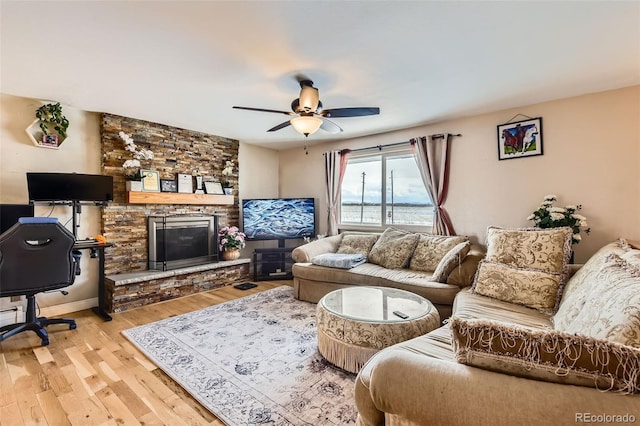 living room featuring a stone fireplace, light hardwood / wood-style flooring, and ceiling fan