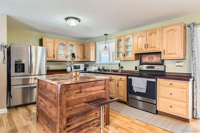 kitchen featuring sink, light hardwood / wood-style flooring, stainless steel appliances, light brown cabinetry, and decorative light fixtures