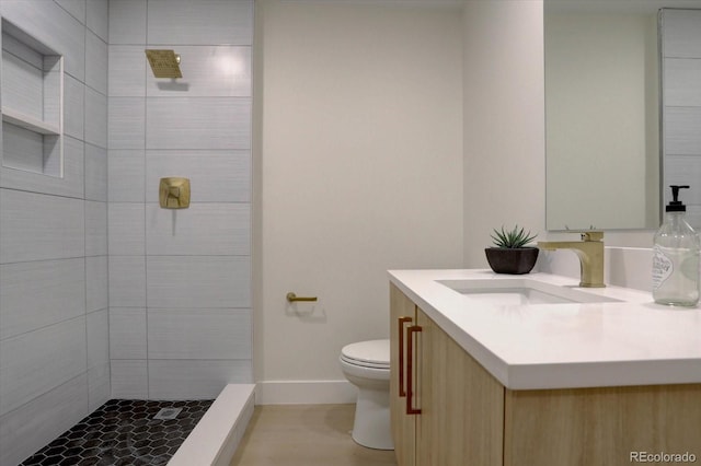 bathroom featuring a tile shower, vanity, and toilet