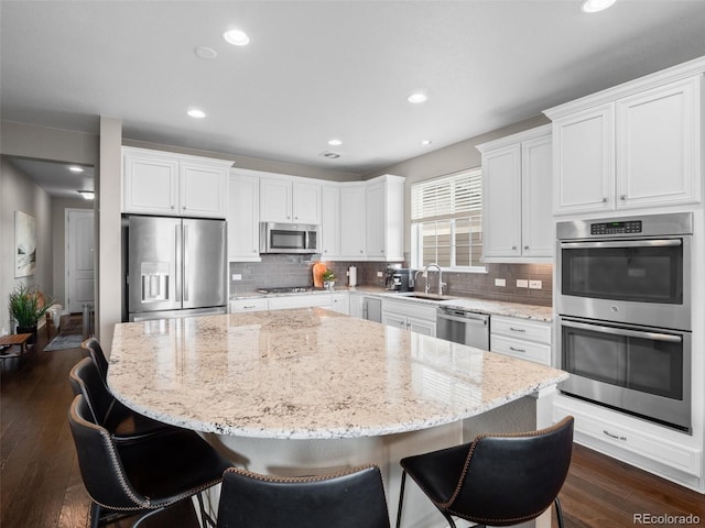 kitchen with white cabinetry, appliances with stainless steel finishes, a kitchen island, and light stone countertops