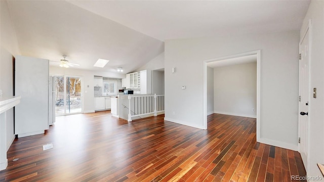 unfurnished living room featuring ceiling fan, vaulted ceiling with skylight, and wood finished floors