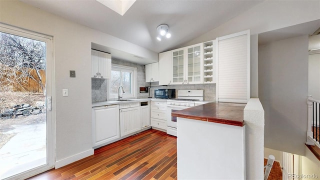 kitchen featuring black microwave, vaulted ceiling with skylight, white gas range, white cabinetry, and a sink