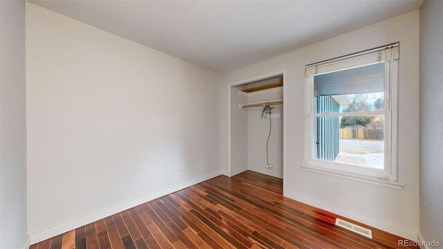 unfurnished bedroom with dark wood-style floors, a closet, visible vents, and baseboards