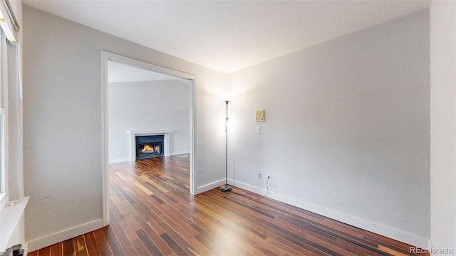 unfurnished room featuring a warm lit fireplace, baseboards, and wood finished floors