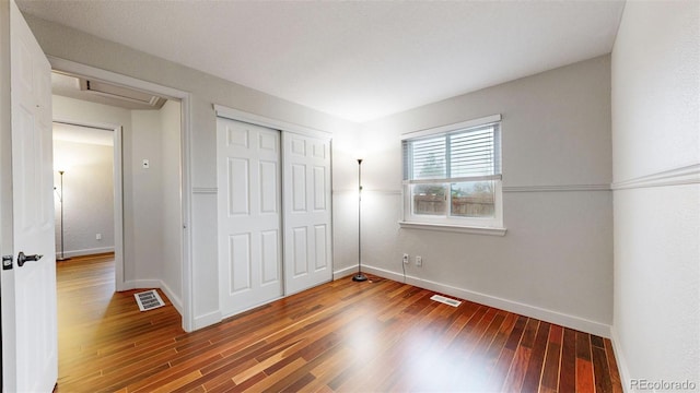 unfurnished bedroom with a closet, visible vents, baseboards, and wood finished floors