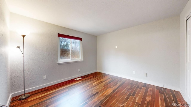 spare room with baseboards, visible vents, wood finished floors, and a textured wall