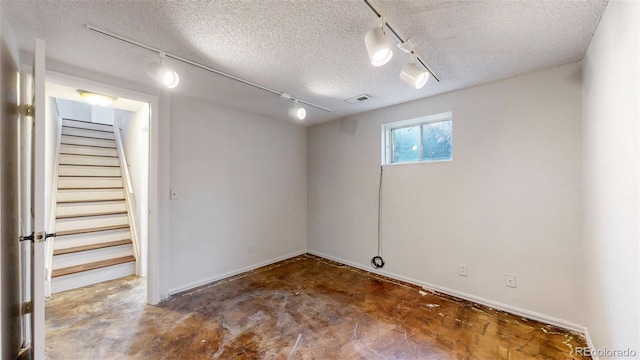 below grade area featuring visible vents, a textured ceiling, track lighting, and stairs