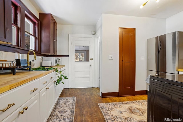 kitchen featuring dark wood-type flooring, freestanding refrigerator, white cabinets, wooden counters, and baseboards