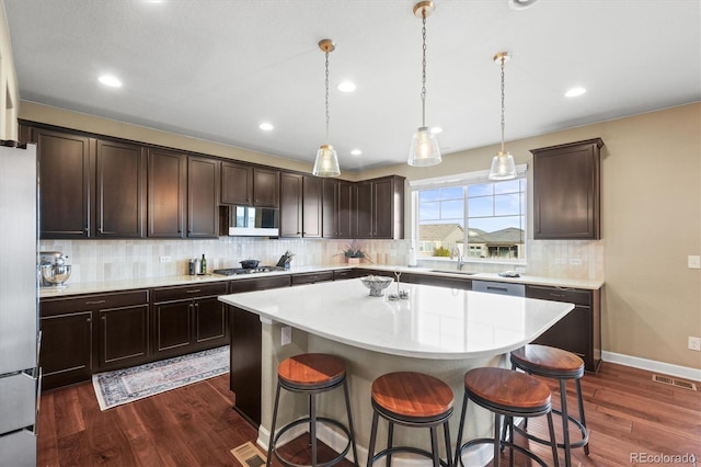 kitchen featuring dark wood finished floors, a breakfast bar, a sink, decorative backsplash, and appliances with stainless steel finishes