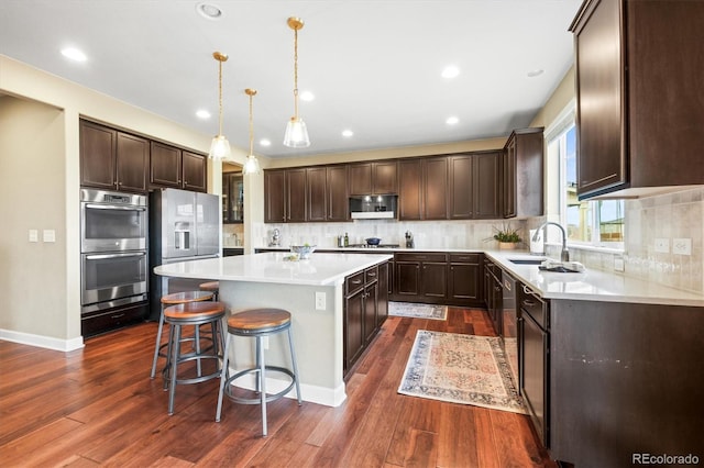 kitchen featuring a sink, a center island, dark brown cabinetry, appliances with stainless steel finishes, and dark wood-style flooring