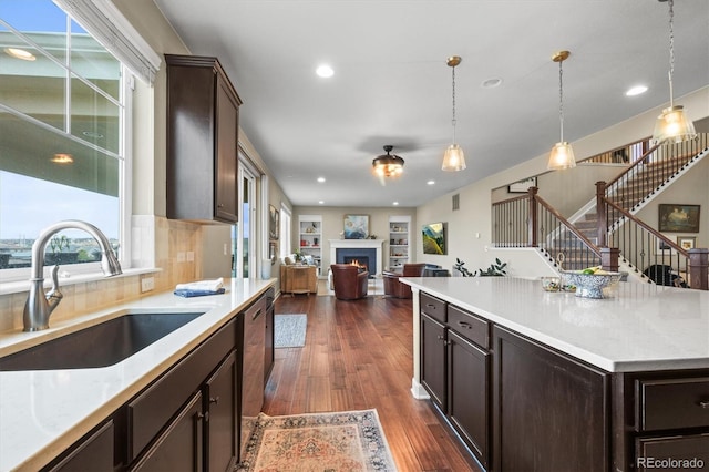 kitchen with dark wood-type flooring, dark brown cabinetry, a warm lit fireplace, and a sink