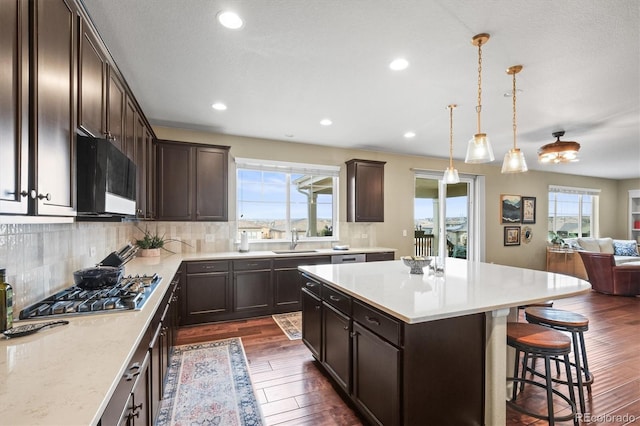 kitchen with a sink, open floor plan, dark wood finished floors, stainless steel gas stovetop, and dark brown cabinets