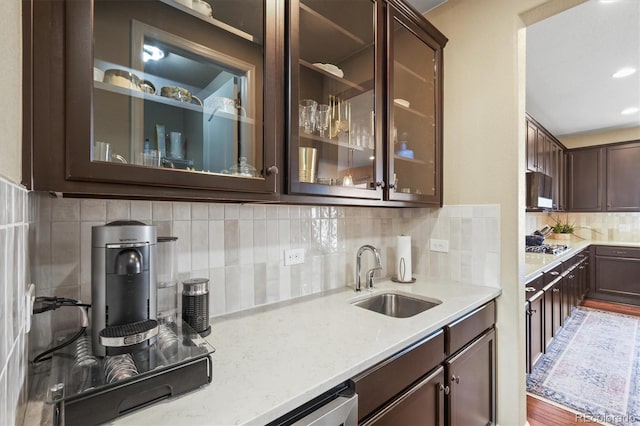 kitchen with glass insert cabinets, light stone countertops, dark brown cabinetry, decorative backsplash, and a sink