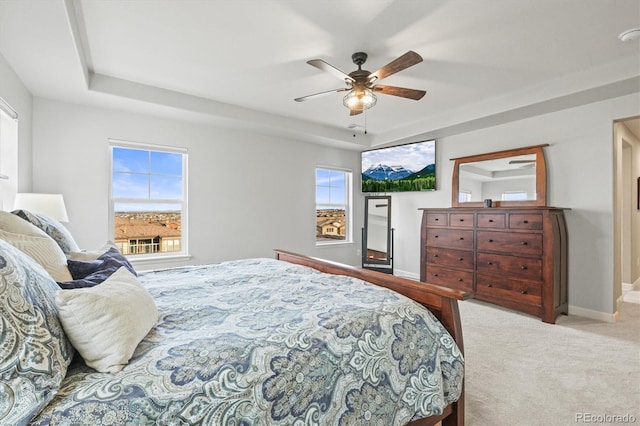 carpeted bedroom featuring a ceiling fan, a tray ceiling, and baseboards