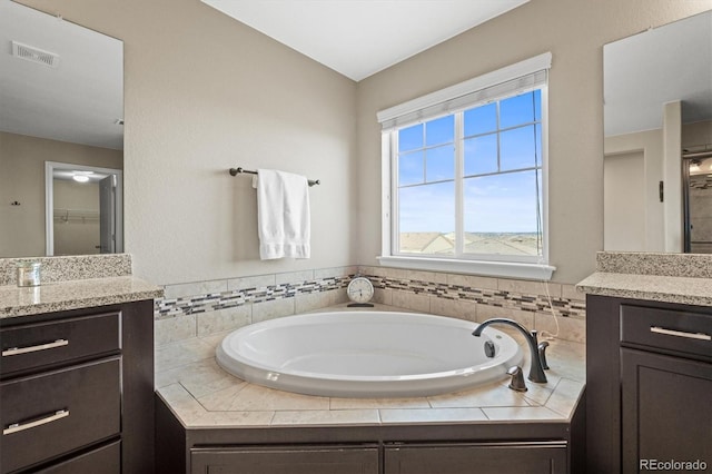 full bathroom featuring a bath, visible vents, vanity, and a walk in closet