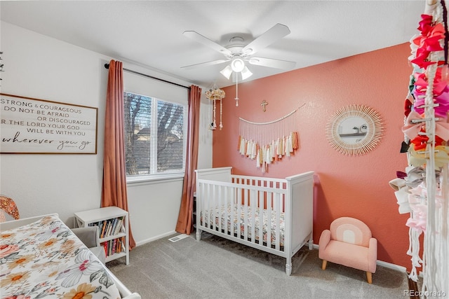 carpeted bedroom with ceiling fan and a crib