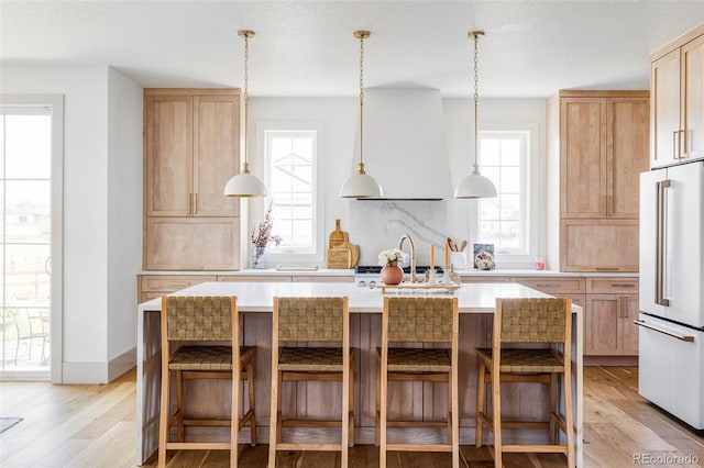 kitchen with light brown cabinetry, high end fridge, a center island, ventilation hood, and light wood-type flooring