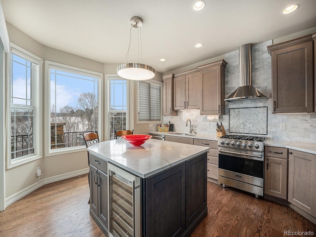 kitchen with wine cooler, stainless steel stove, sink, wall chimney range hood, and pendant lighting