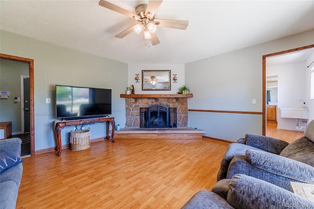 14347 E 134th Ave, Brighton, CO 80601 - living room featuring light wood-style floors, a ceiling fan, a stone fireplace, and baseboards