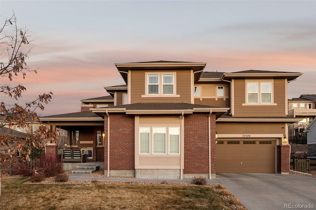 prairie-style home with an attached garage, covered porch, brick siding, and driveway