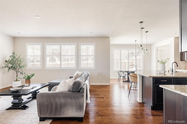 living area featuring an inviting chandelier, baseboards, and dark wood-style flooring