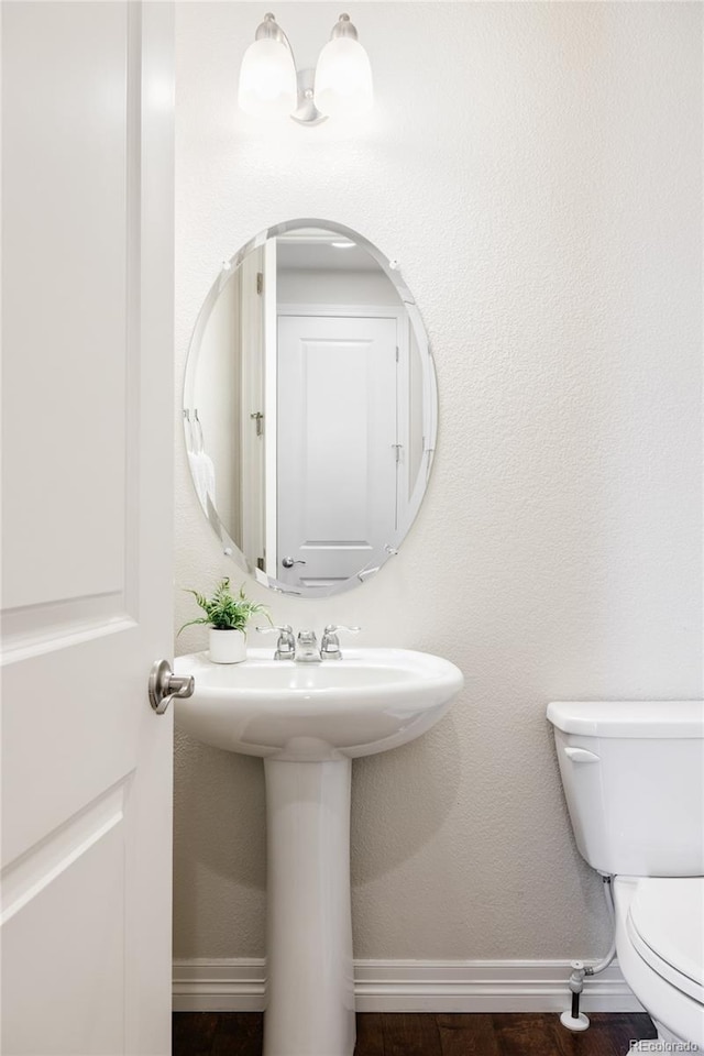 half bathroom featuring toilet, wood finished floors, and baseboards