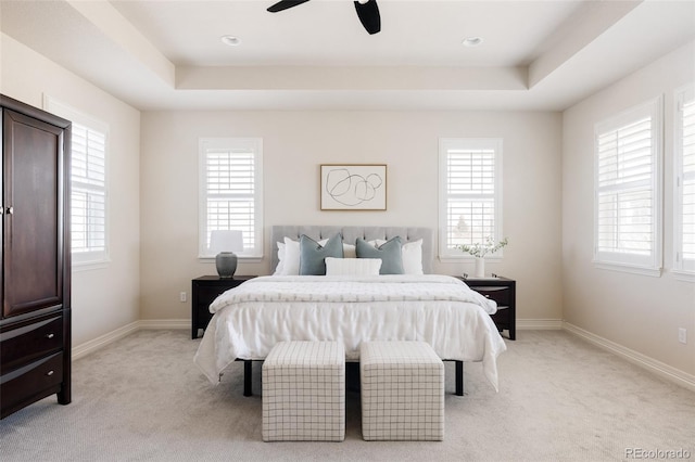 bedroom featuring a ceiling fan, a tray ceiling, light colored carpet, and baseboards