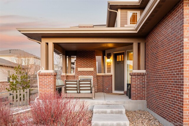 view of exterior entry featuring brick siding and a porch