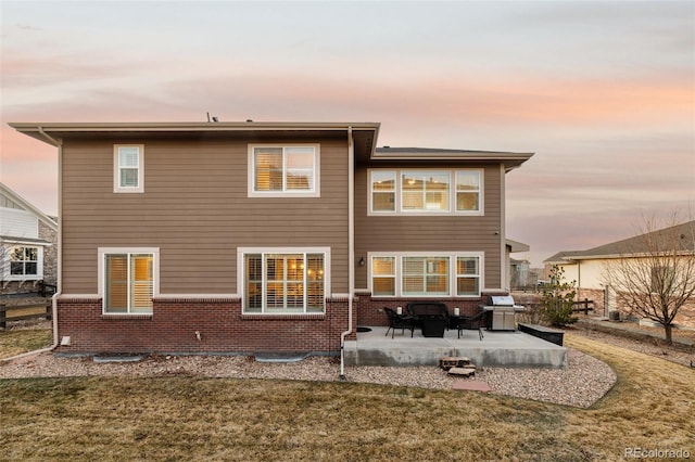 back of house with a patio area, a lawn, and brick siding