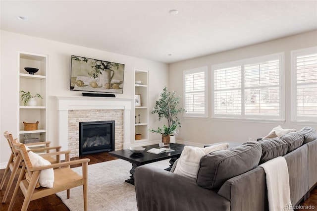 living area with built in features, baseboards, dark wood-type flooring, and a stone fireplace