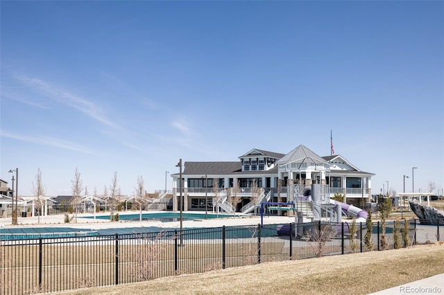 rear view of property with a community pool, stairs, and fence