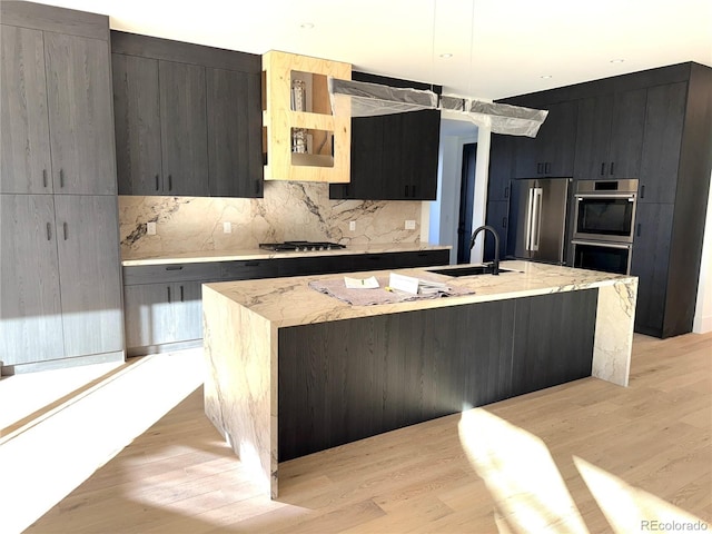 kitchen featuring a kitchen island with sink, sink, light hardwood / wood-style flooring, and appliances with stainless steel finishes