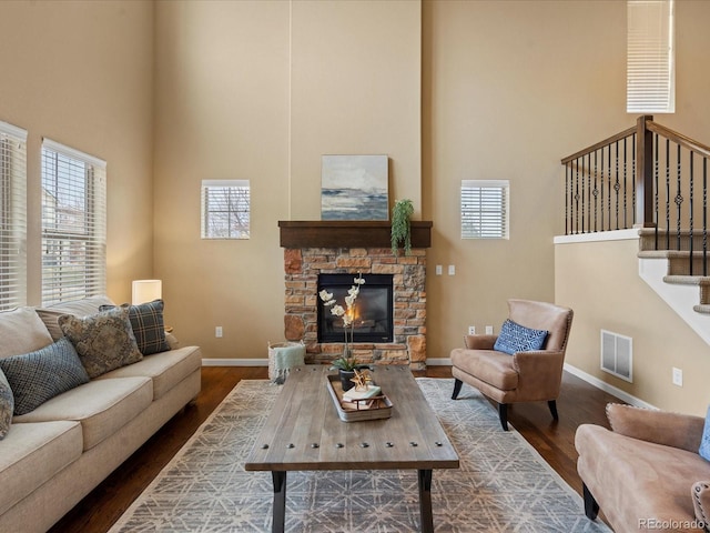 living area with baseboards, visible vents, dark wood finished floors, a high ceiling, and a stone fireplace