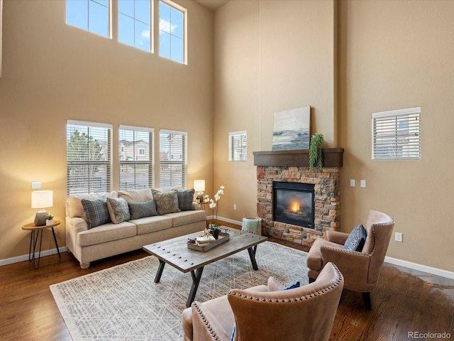 living room featuring a fireplace, wood finished floors, baseboards, and a towering ceiling