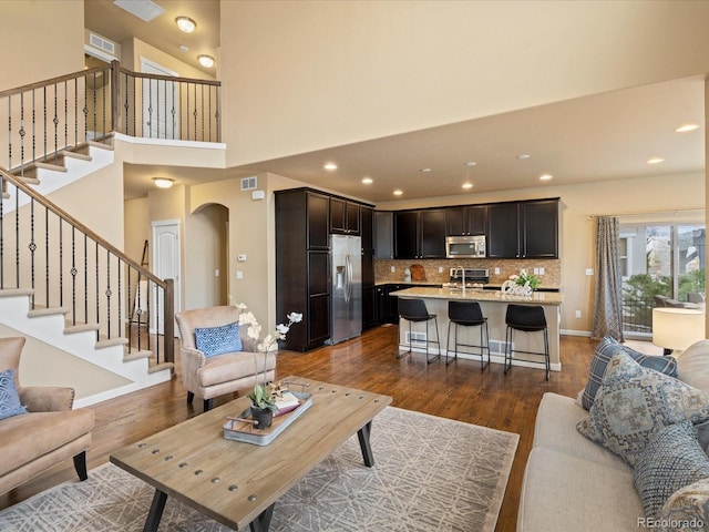 living room featuring stairway, baseboards, a high ceiling, arched walkways, and dark wood-type flooring