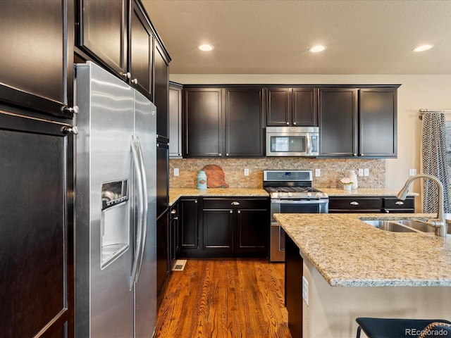 kitchen featuring tasteful backsplash, a sink, light stone counters, stainless steel appliances, and dark wood-style flooring