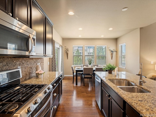 kitchen with light stone counters, a sink, stainless steel appliances, dark wood-type flooring, and backsplash