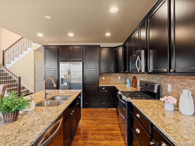 kitchen with a sink, tasteful backsplash, dark wood-style floors, stainless steel appliances, and light stone countertops