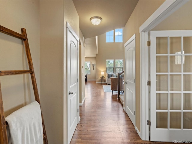 hall featuring baseboards, a high ceiling, and wood finished floors