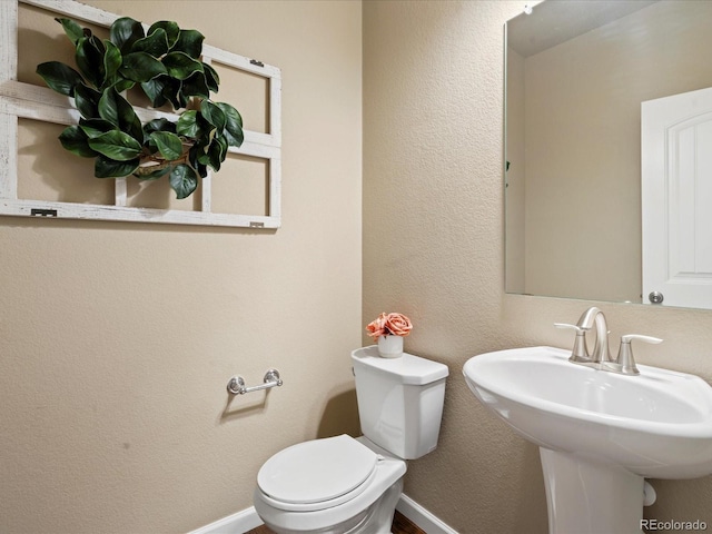 half bathroom featuring a sink, baseboards, toilet, and a textured wall