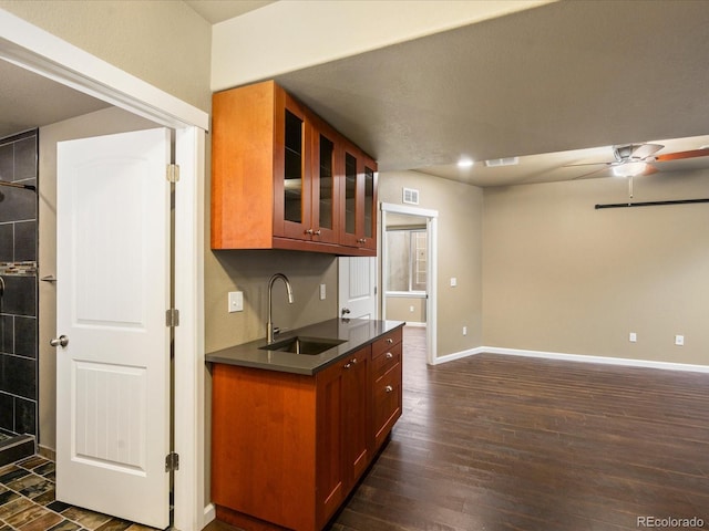 kitchen with baseboards, dark wood finished floors, ceiling fan, a sink, and glass insert cabinets