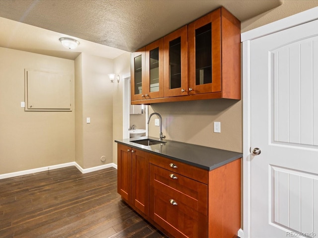 kitchen with dark countertops, glass insert cabinets, baseboards, dark wood-style floors, and a sink