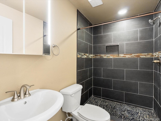 full bath featuring a sink, tiled shower, and toilet