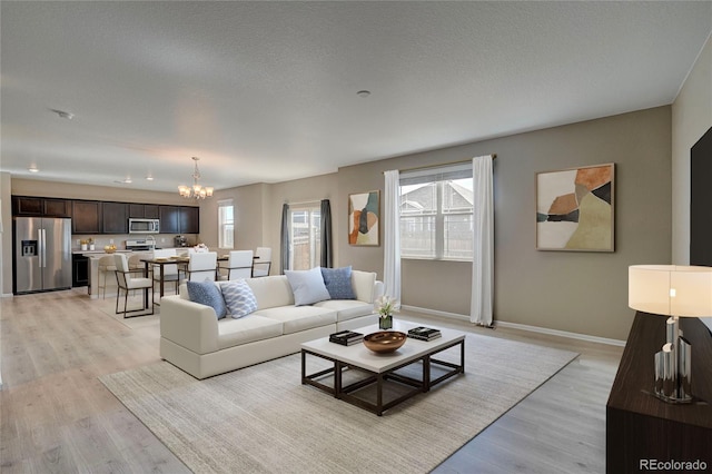 living area featuring light wood finished floors, plenty of natural light, a textured ceiling, and a chandelier