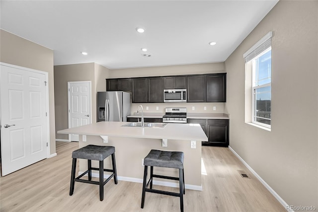 kitchen with a breakfast bar area, an island with sink, appliances with stainless steel finishes, light wood-style floors, and a sink